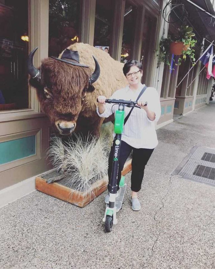 Lorie McDonald rides a scooter in front of a buffalo prop.